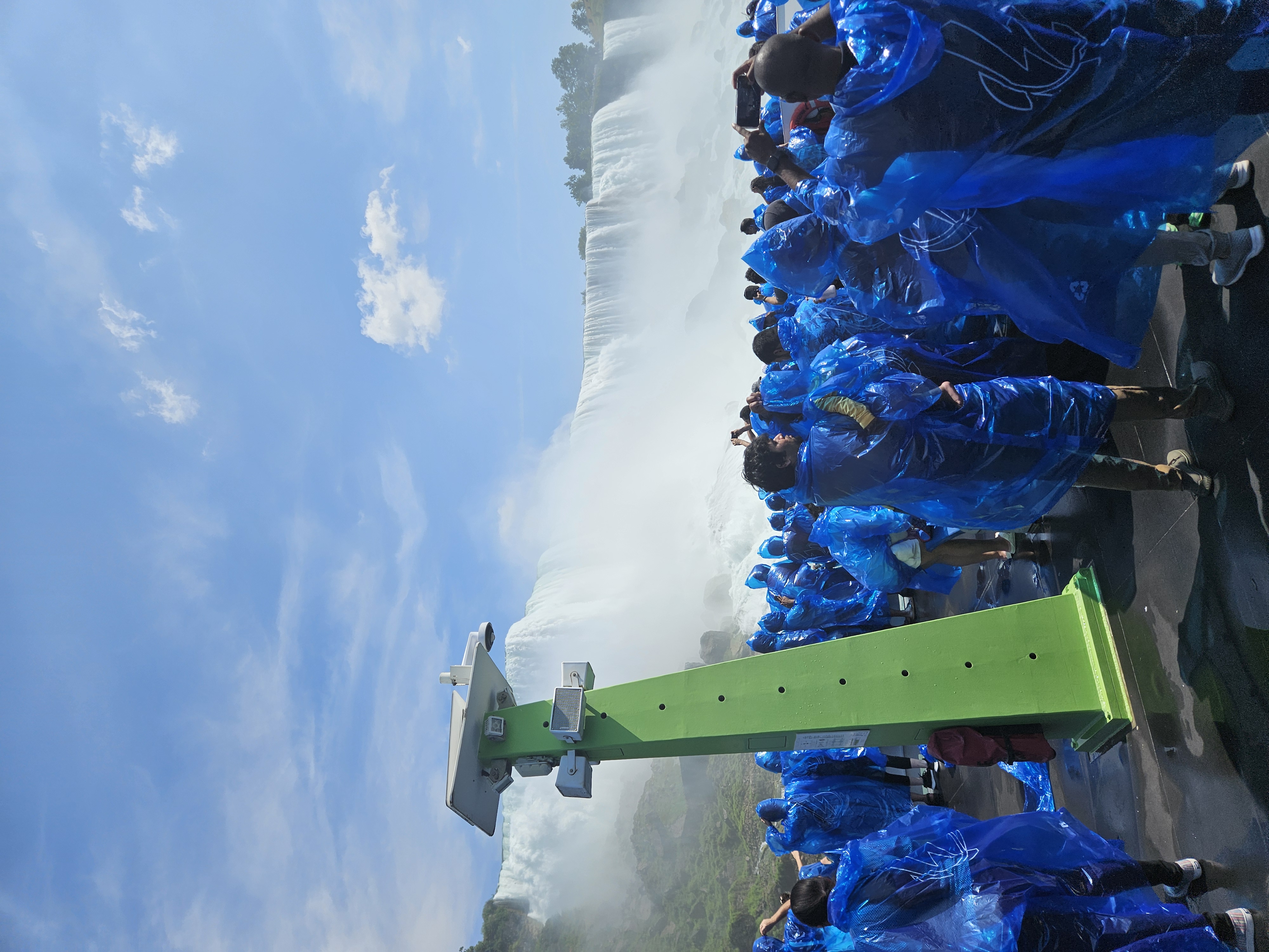 Tourists in blue ponchos crowd the deck near the mist and rushing water of Niagara Falls.