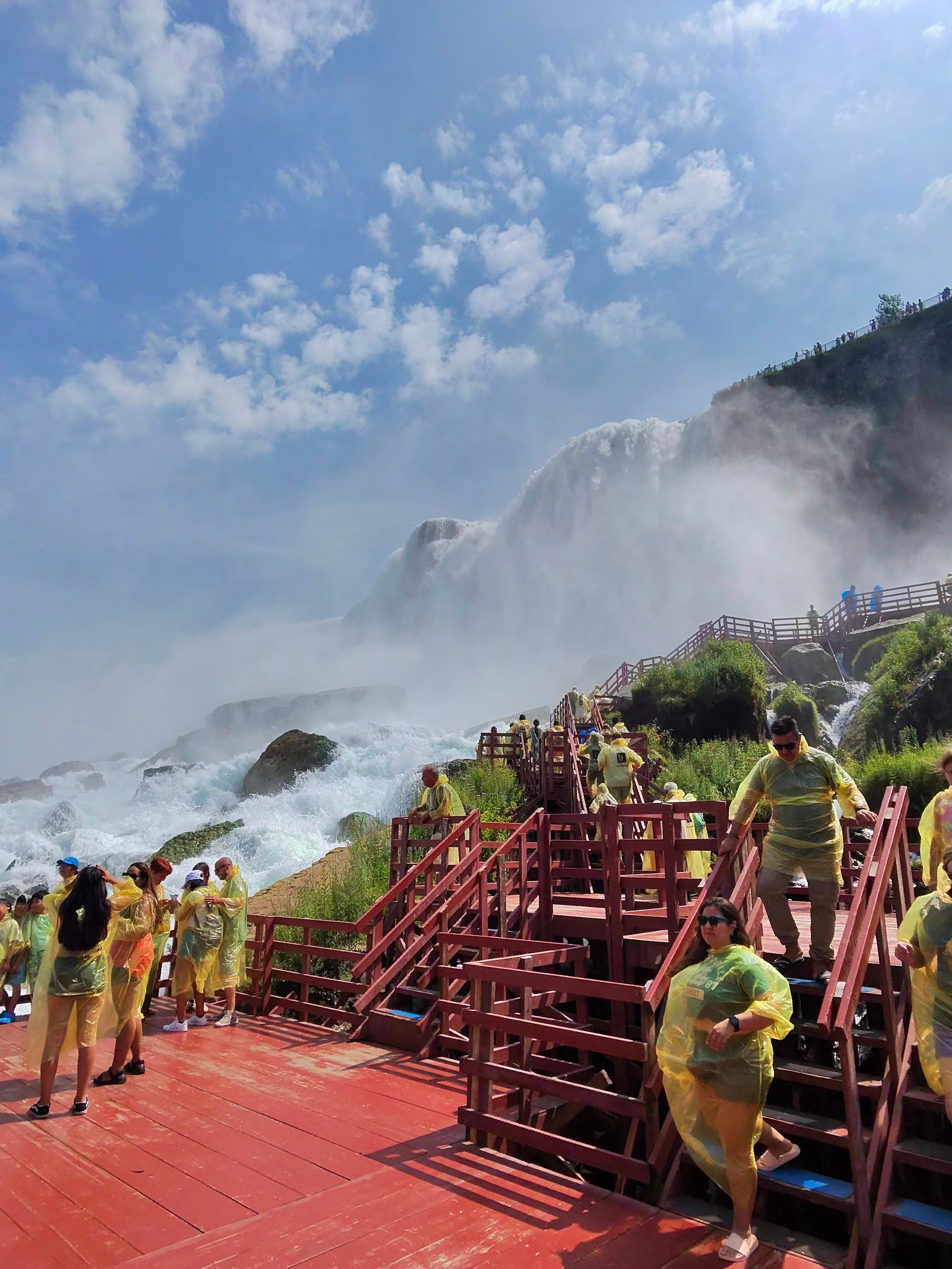 Visitors in ponchos descend the red wooden boardwalk beside the mist and rushing water of Niagara Falls.